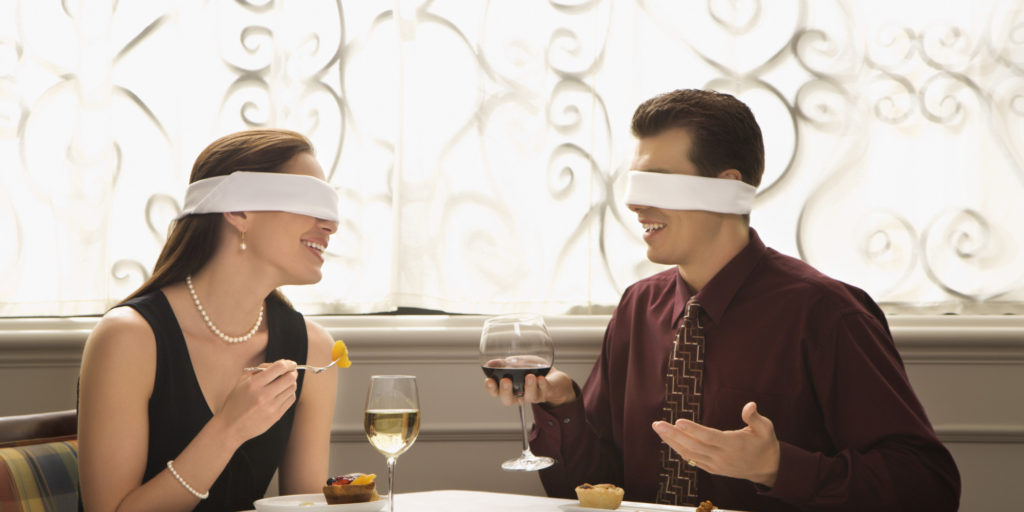 Mid adult Caucasian couple dining in a restaurant with blindfolds over eyes.